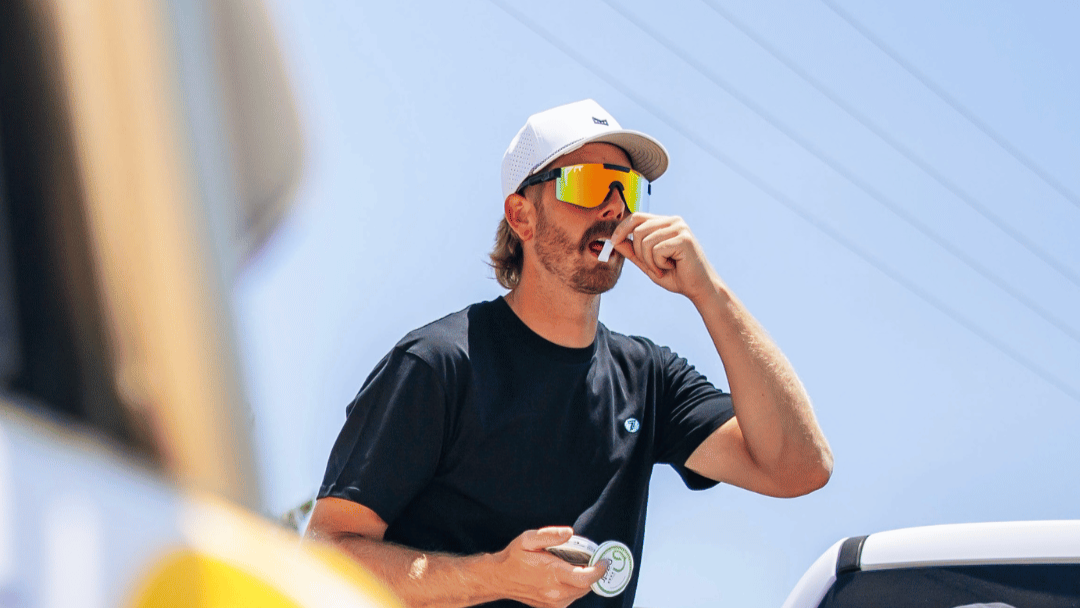 Man sitting in a car wearing sunglasses and a cap, with a blurred background