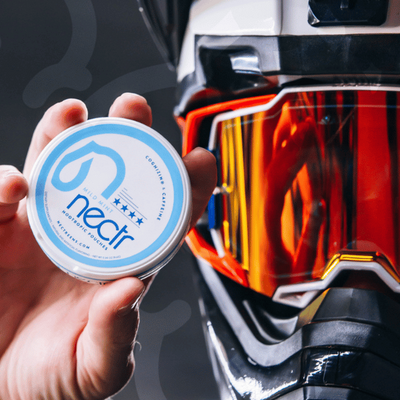 Hand holding a container labeled 'nectr' in front of a reflective surface.